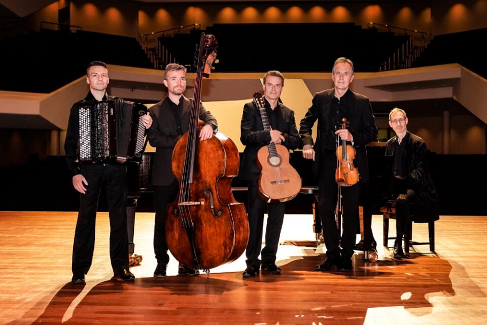 5 men stand together looking at the camera, in a concert hall